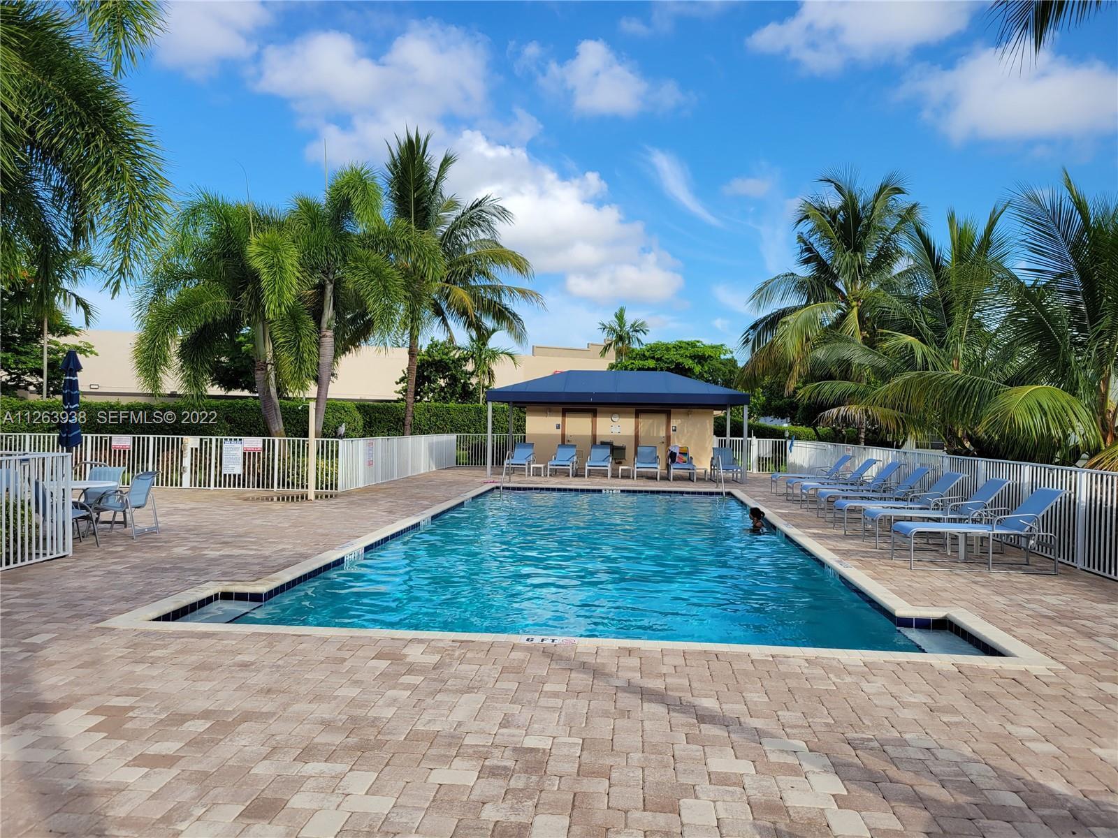 A rectangular swimming pool is surrounded by lounge chairs and palm trees under a blue sky — 9826 Marina Boulevard # 1015, Boca Raton FL 33428, BOCA RATON, FL