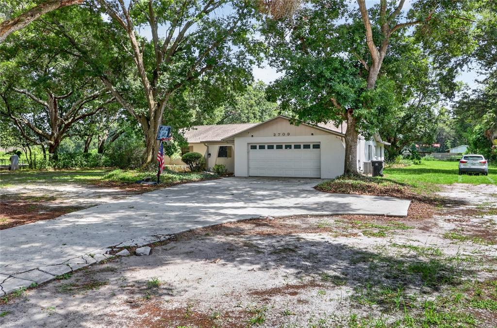 A single-story house with a white garage door, concrete driveway, and large shade trees — 2709 W SAM ALLEN ROAD, PLANT CITY, FL