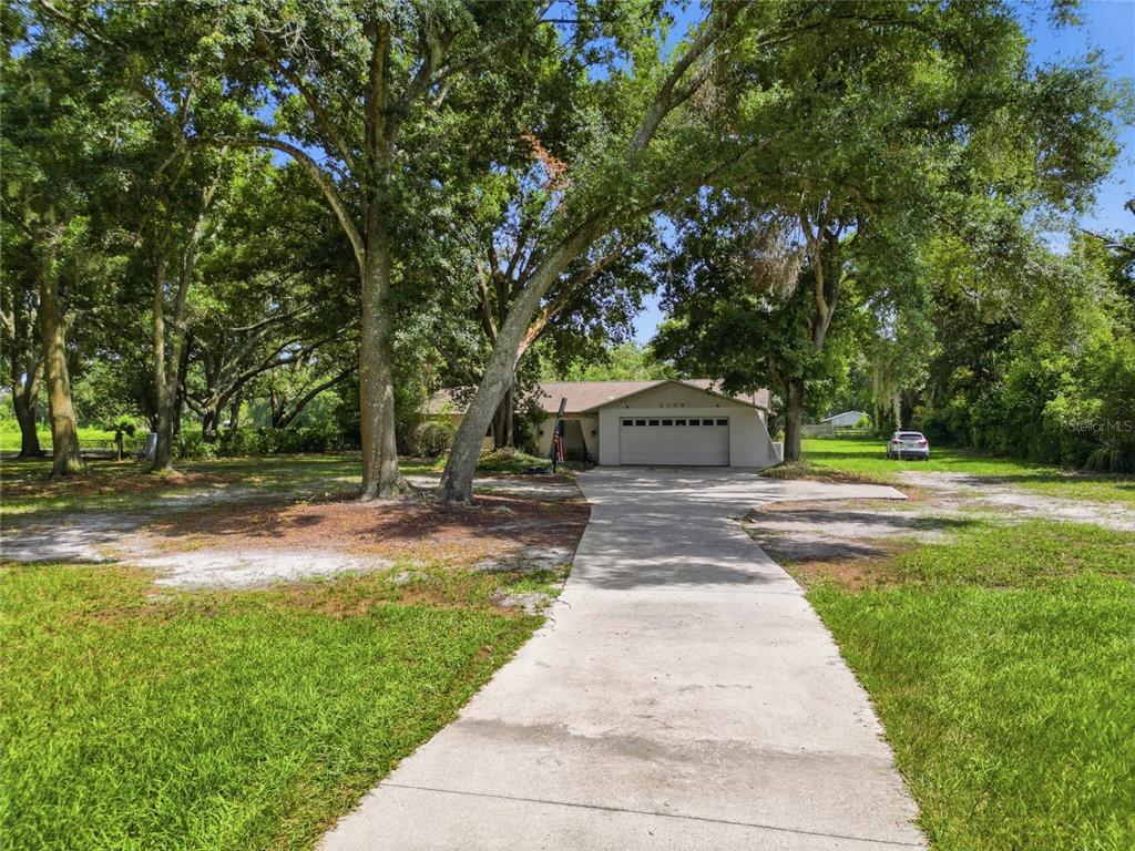A concrete driveway leads to a single-story house with a two-car garage under large trees — 2709 W SAM ALLEN ROAD, PLANT CITY, FL