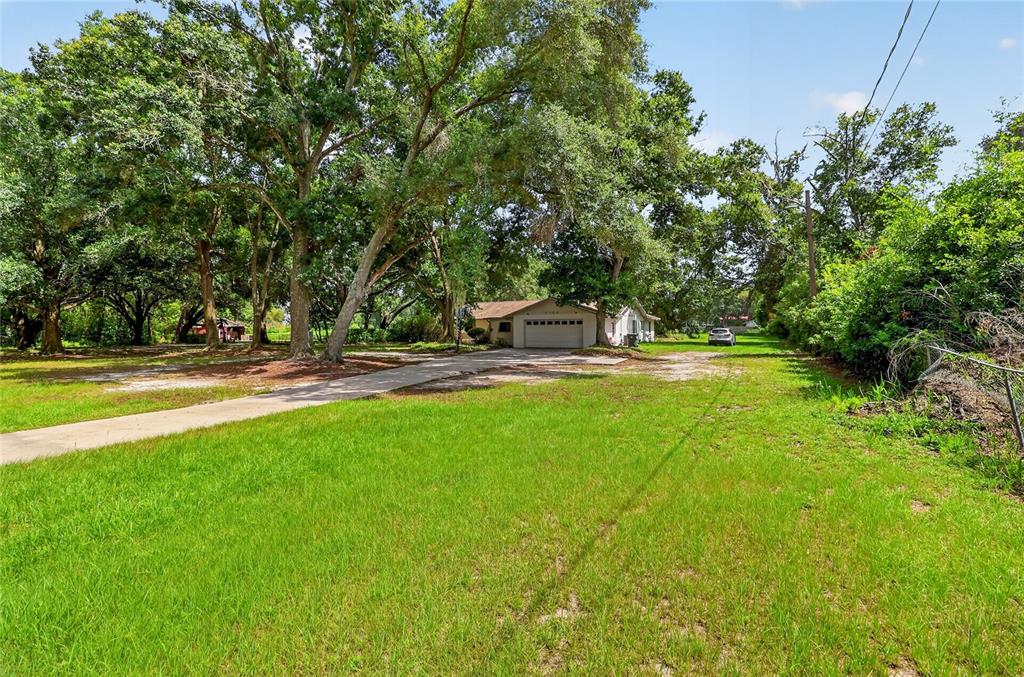 A single-story house with a garage sits on a large, grassy lot with many trees — 2709 W SAM ALLEN ROAD, PLANT CITY, FL
