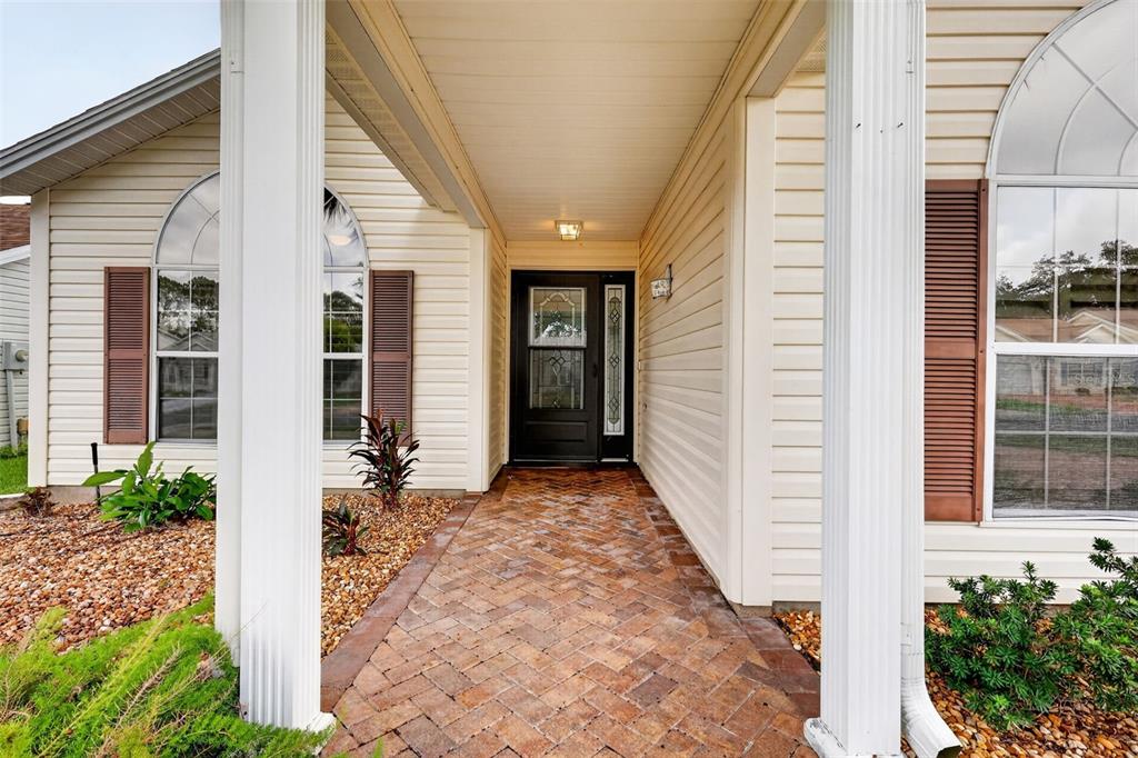 A brick walkway leads to the front door of a house with beige vinyl siding — 2129 MARGARITA DRIVE, THE VILLAGES, FL