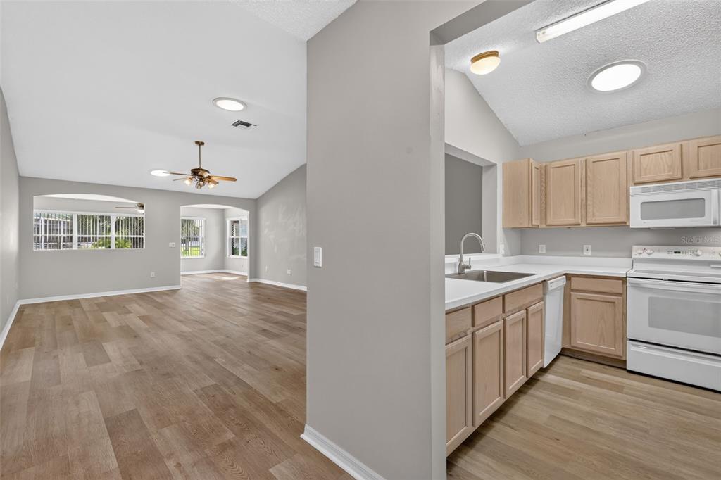 A kitchen with light wood cabinets and white appliances opens into a spacious living area — 2129 MARGARITA DRIVE, THE VILLAGES, FL