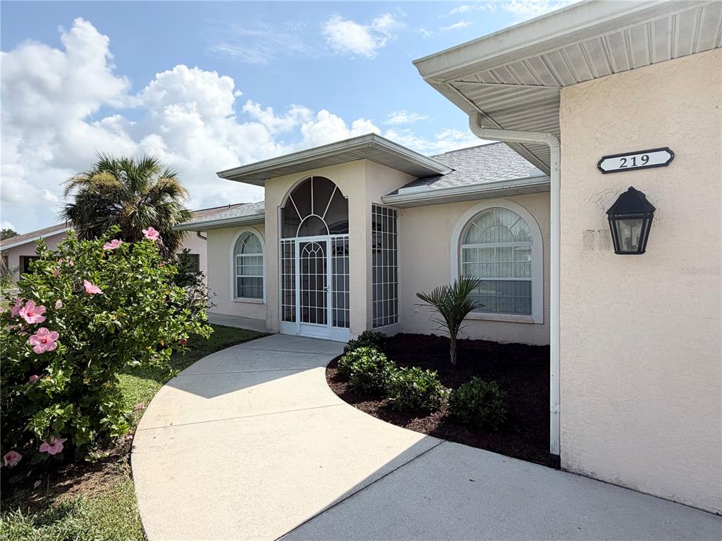 A concrete walkway leads to the front entrance of a light-colored house with arched windows — 219 VENETIA AVENUE, NORTH PORT, FL