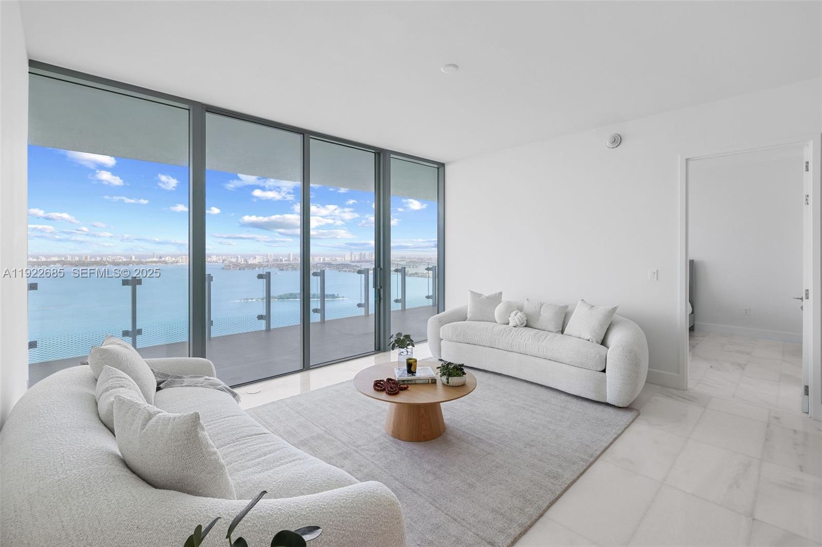 A living room features two white sofas, a round wooden coffee table, and floor-to-ceiling windows — 700 NE 26 Ter # 3602, Miami FL 33137, MIAMI, FL