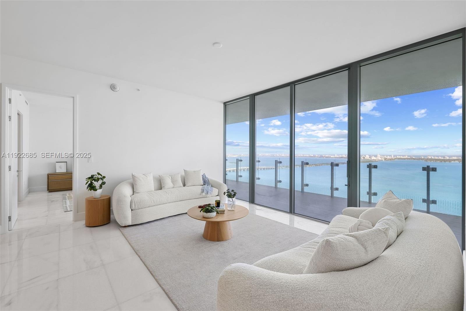 A modern living room features white sofas, a round coffee table, and floor-to-ceiling windows — 700 NE 26 Ter # 3602, Miami FL 33137, MIAMI, FL