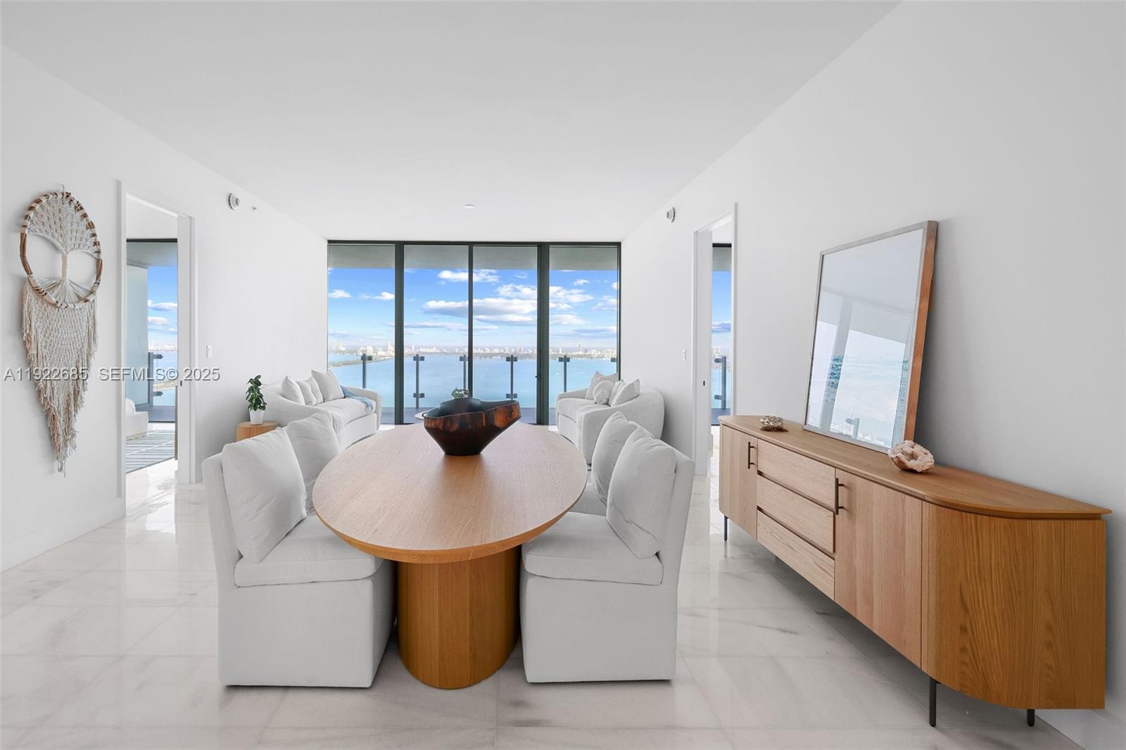 A dining room features an oval wooden table, white upholstered chairs, and floor-to-ceiling windows — 700 NE 26 Ter # 3602, Miami FL 33137, MIAMI, FL
