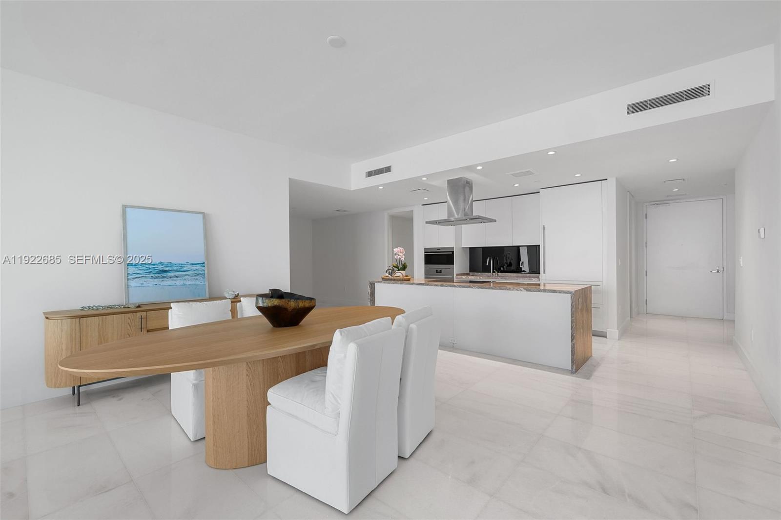 A modern open-concept kitchen and dining area features white cabinetry, a wooden table, and marble flooring — 700 NE 26 Ter # 3602, Miami FL 33137, MIAMI, FL