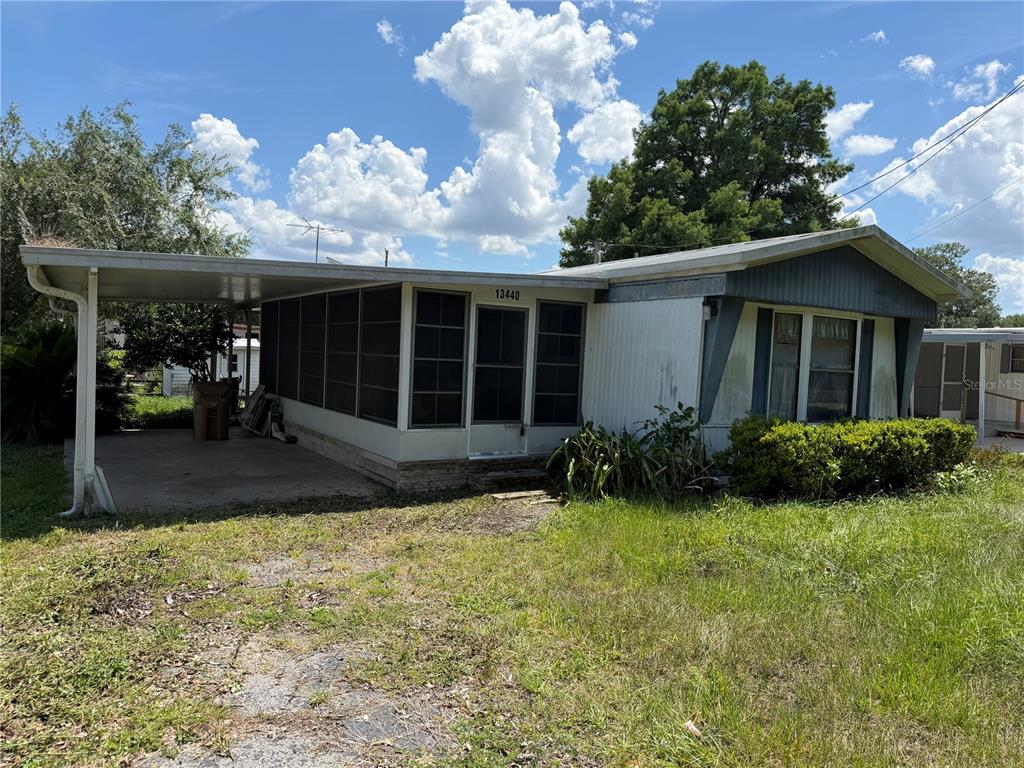 A single-story mobile home features a screened-in porch, a carport, and an overgrown grassy yard — 13440 PALM DRIVE UNIT 7, ASTATULA, FL