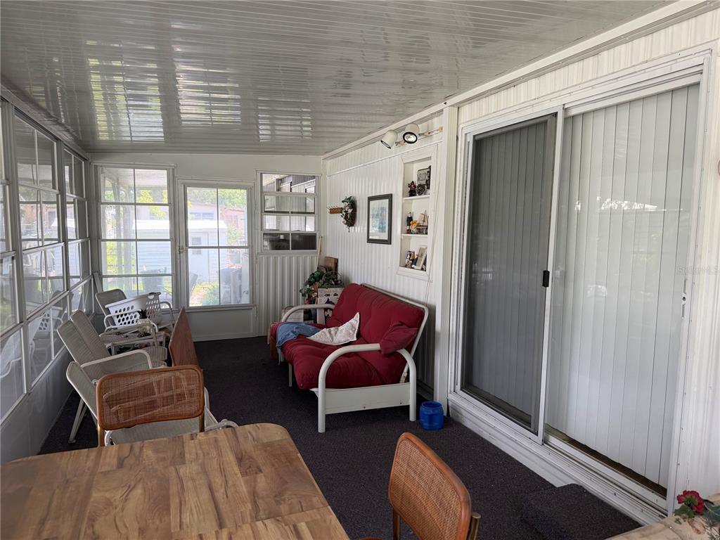 A sunroom features a red futon, wicker chairs, a wooden table, and sliding glass doors — 13440 PALM DRIVE UNIT 7, ASTATULA, FL