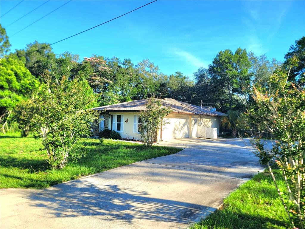 A single-story house with a concrete driveway and surrounding trees under a clear blue sky — 19725 SW BEACH BOULEVARD, DUNNELLON, FL
