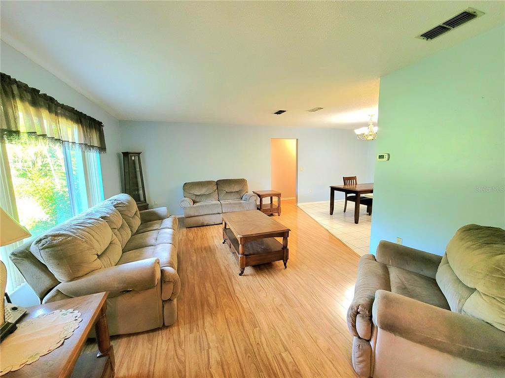 A living room features light wood flooring, light blue walls, and three beige sofas — 19725 SW BEACH BOULEVARD, DUNNELLON, FL
