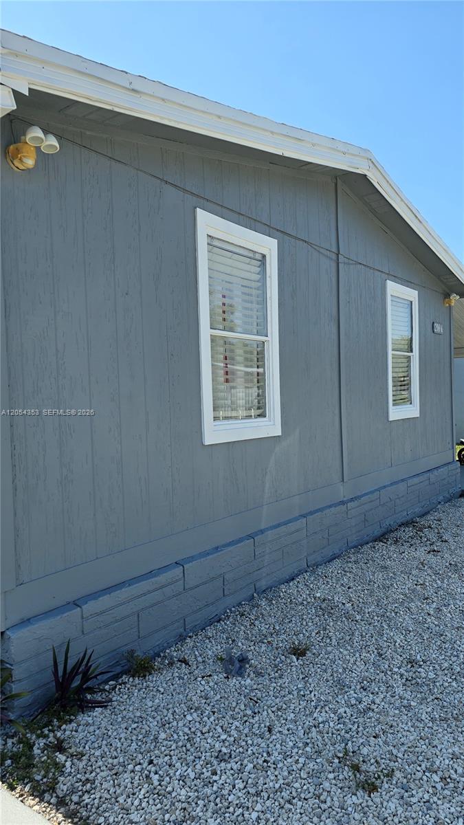 The exterior of a gray manufactured home features vertical siding, white-trimmed windows, and a gravel yard — 20016 NW 56 Ave, Miami Gardens FL 33055, MIAMI GARDENS, FL