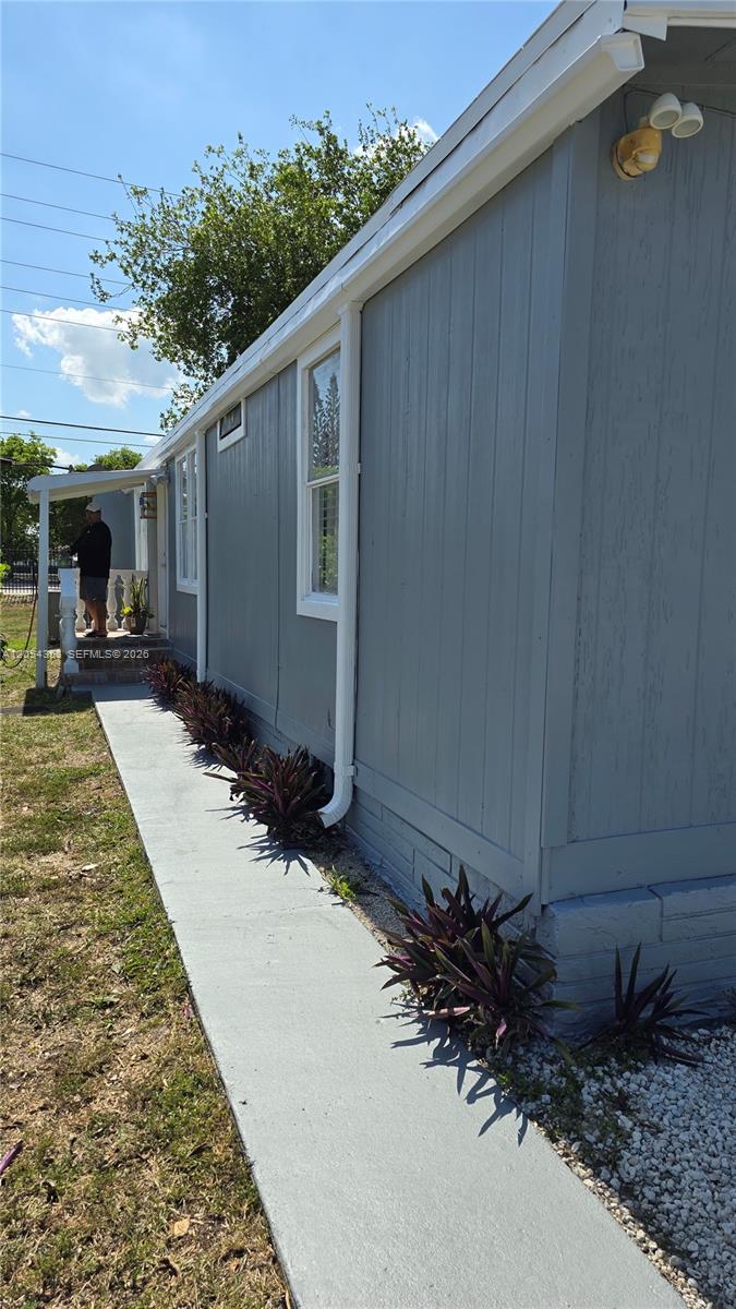 The exterior of a gray house features a concrete walkway lined with purple plants — 20016 NW 56 Ave, Miami Gardens FL 33055, MIAMI GARDENS, FL