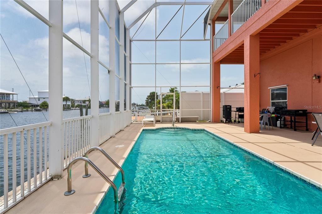 A screened-in pool patio overlooks a canal with a view of neighboring houses — 3294 MINNOW CREEK DRIVE, HERNANDO BEACH, FL
