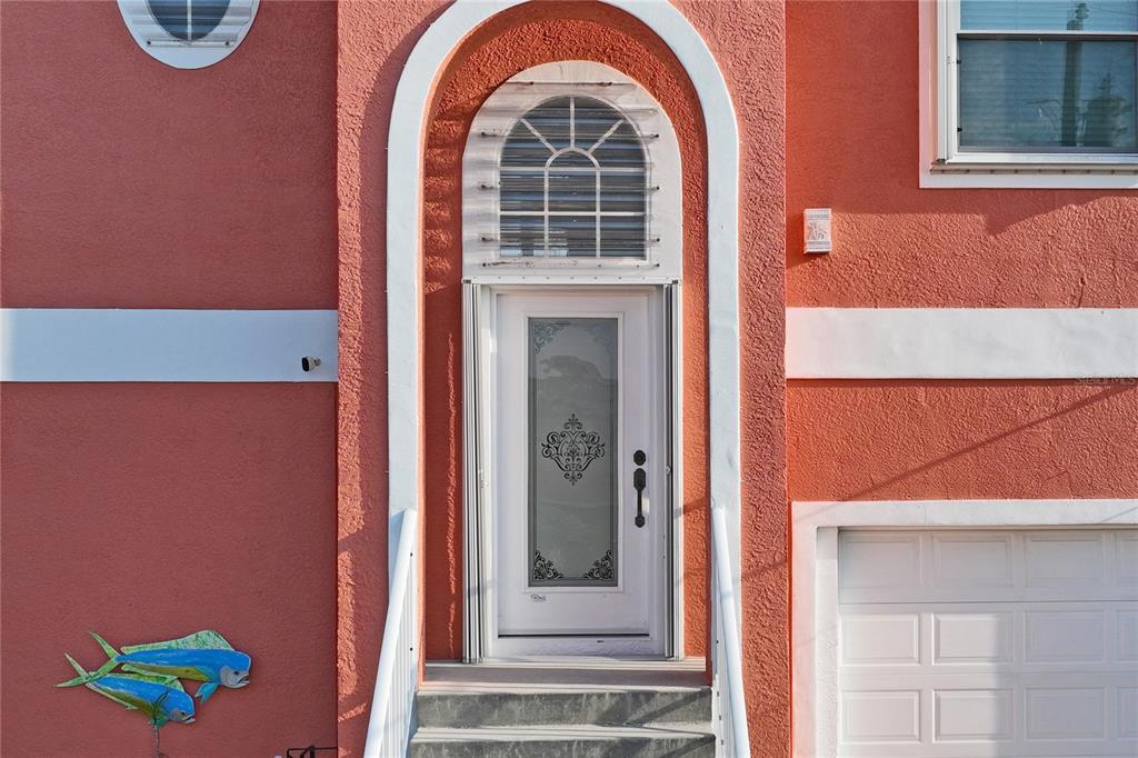 The exterior of a coral-colored house features an arched front door and a decorative fish ornament — 3294 MINNOW CREEK DRIVE, HERNANDO BEACH, FL