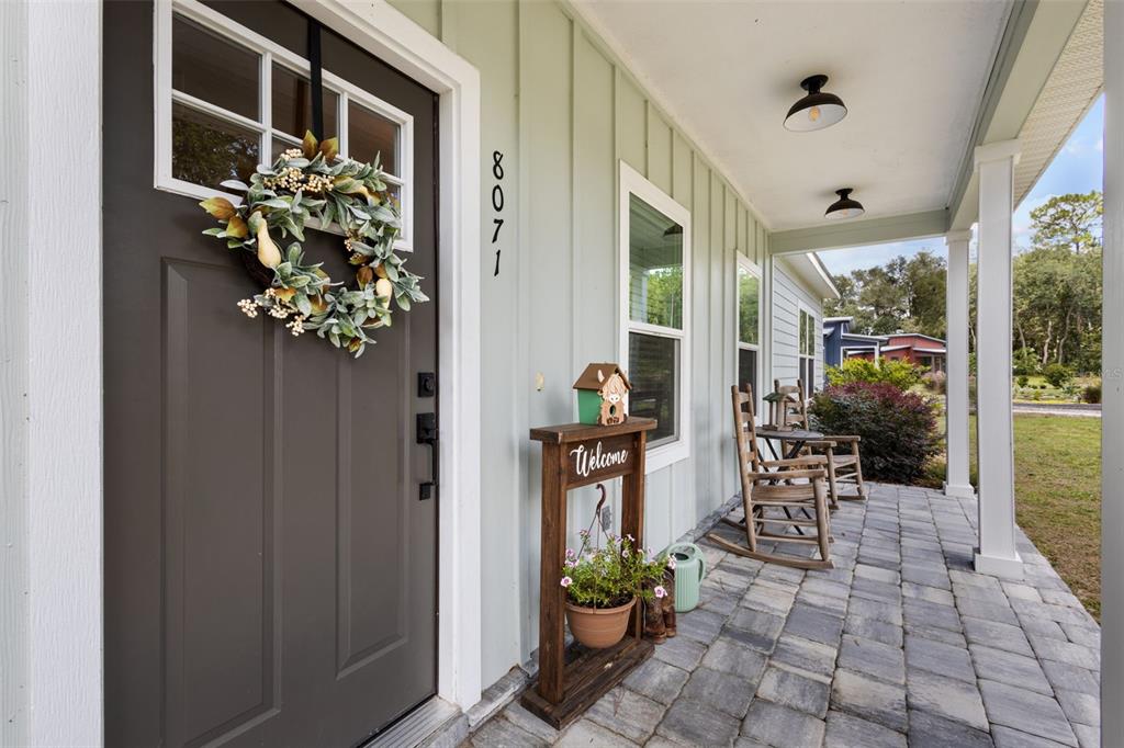 A covered front porch features a dark gray door, rocking chairs, and a stone-paver floor — 8071 NW 172ND LANE, TRENTON, FL