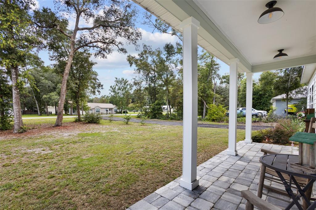 A covered porch with stone pavers overlooks a grassy yard with trees and a driveway — 8071 NW 172ND LANE, TRENTON, FL