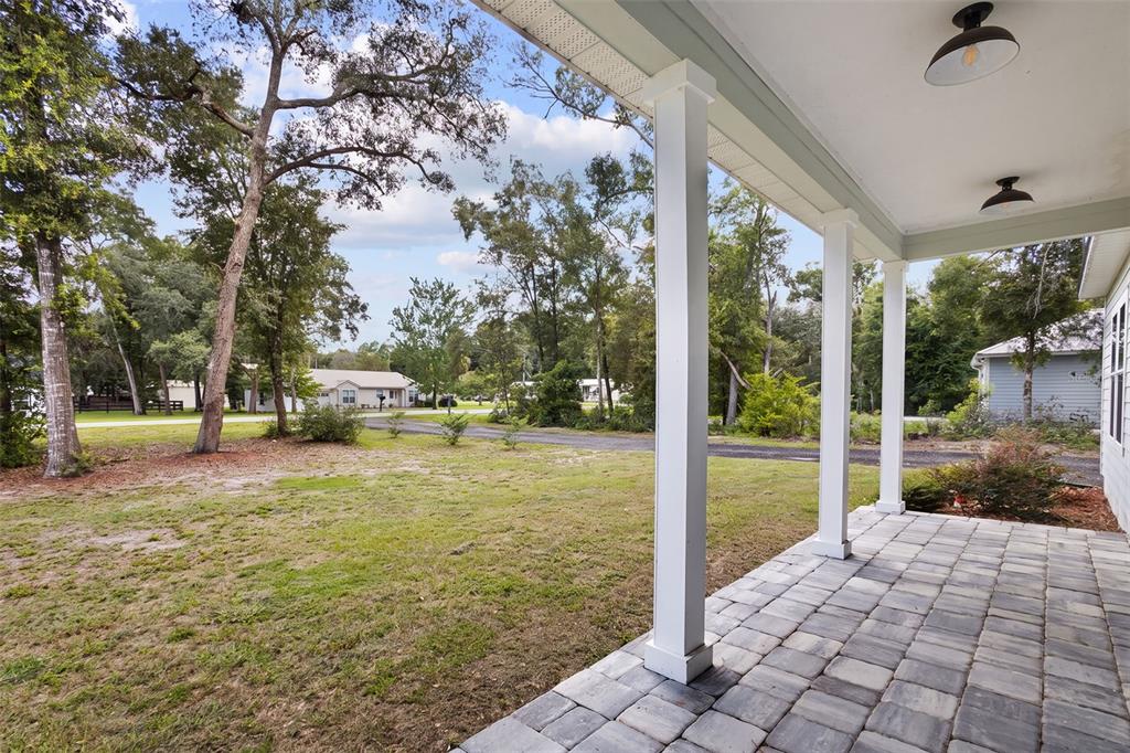 A covered porch with stone pavers overlooks a grassy yard and surrounding trees — 8071 NW 172ND LANE, TRENTON, FL