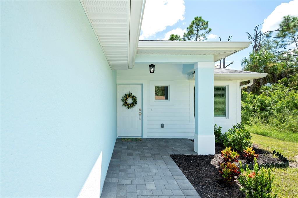 The exterior of a light blue house features a covered entryway with a paved walkway — 2098 COMO STREET, PORT CHARLOTTE, FL