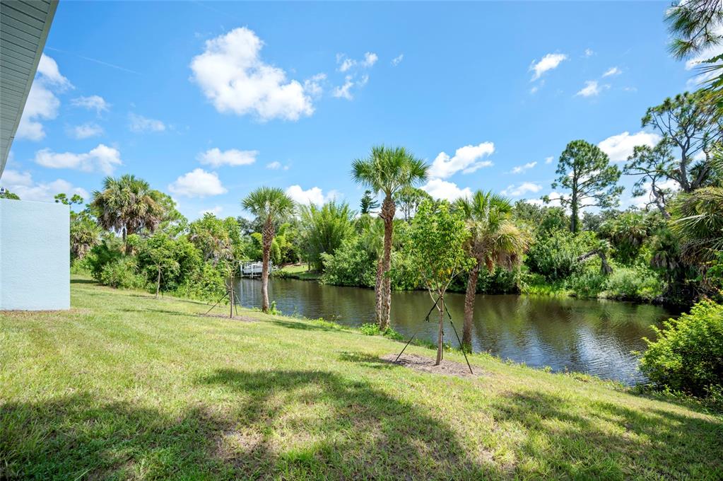 A grassy backyard slopes down toward a canal lined with palm trees and dense vegetation — 2098 COMO STREET, PORT CHARLOTTE, FL