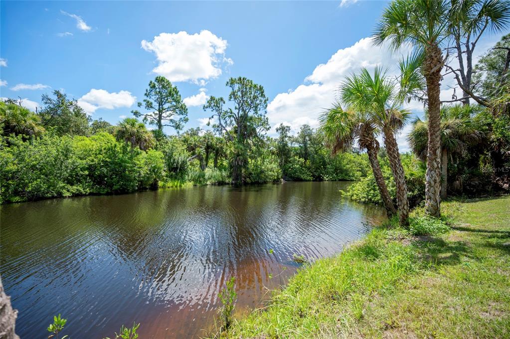 A calm pond is surrounded by lush green trees and palm trees under a blue sky — 2098 COMO STREET, PORT CHARLOTTE, FL