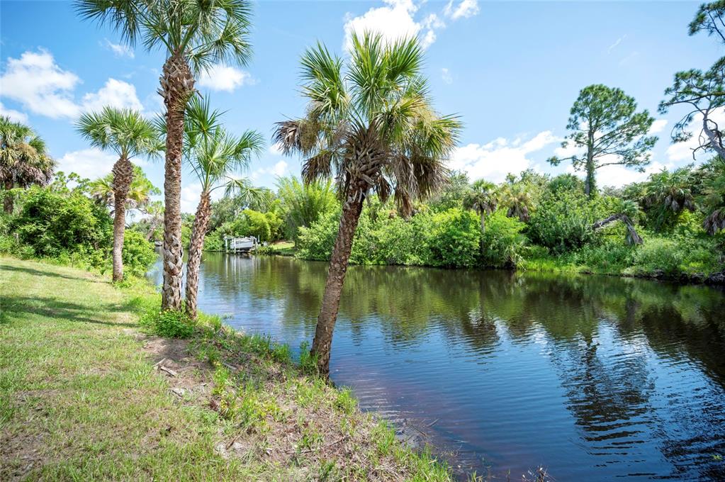 A narrow canal flows past a grassy bank lined with several tall palm trees — 2098 COMO STREET, PORT CHARLOTTE, FL
