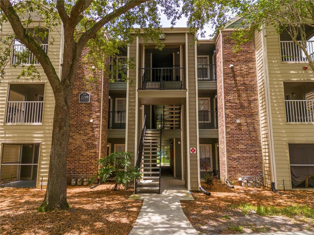 An exterior view of a three-story apartment building with brick siding and outdoor staircases — 2210 YANKEE PLACE UNIT 316, ORLANDO, FL