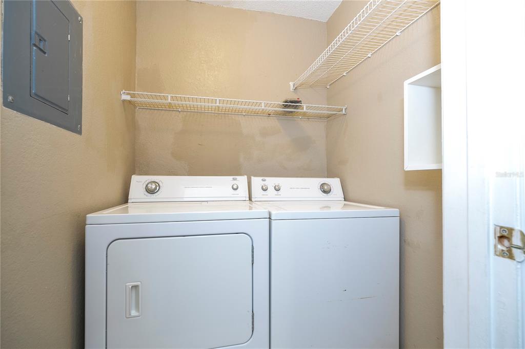 A laundry closet contains a white washer and dryer beneath two wire shelves — 2210 YANKEE PLACE UNIT 316, ORLANDO, FL