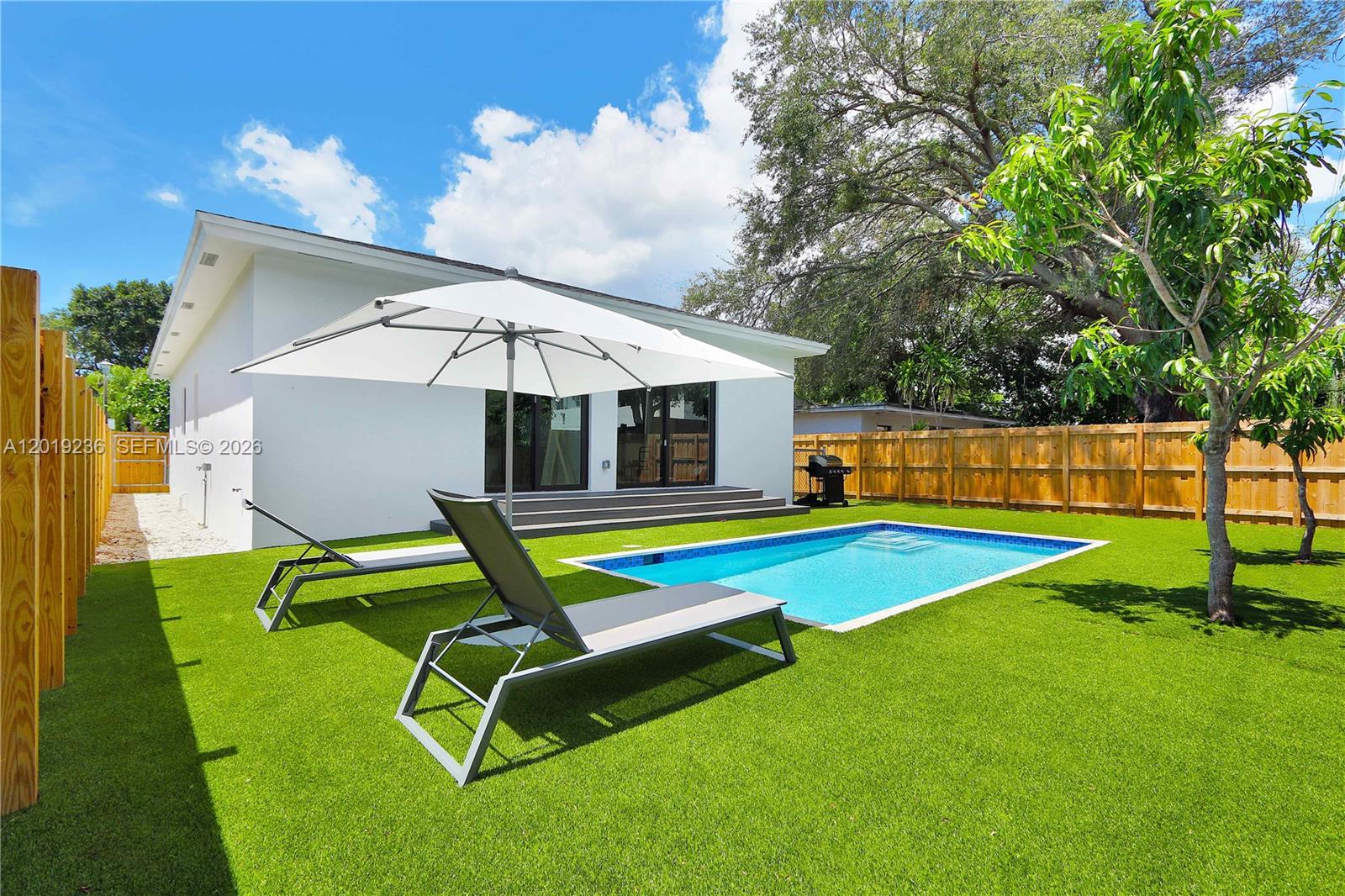 A backyard features a swimming pool, lounge chairs, a white umbrella, and a wooden fence — 2001 SW 22nd Ter, Miami FL 33145, MIAMI, FL