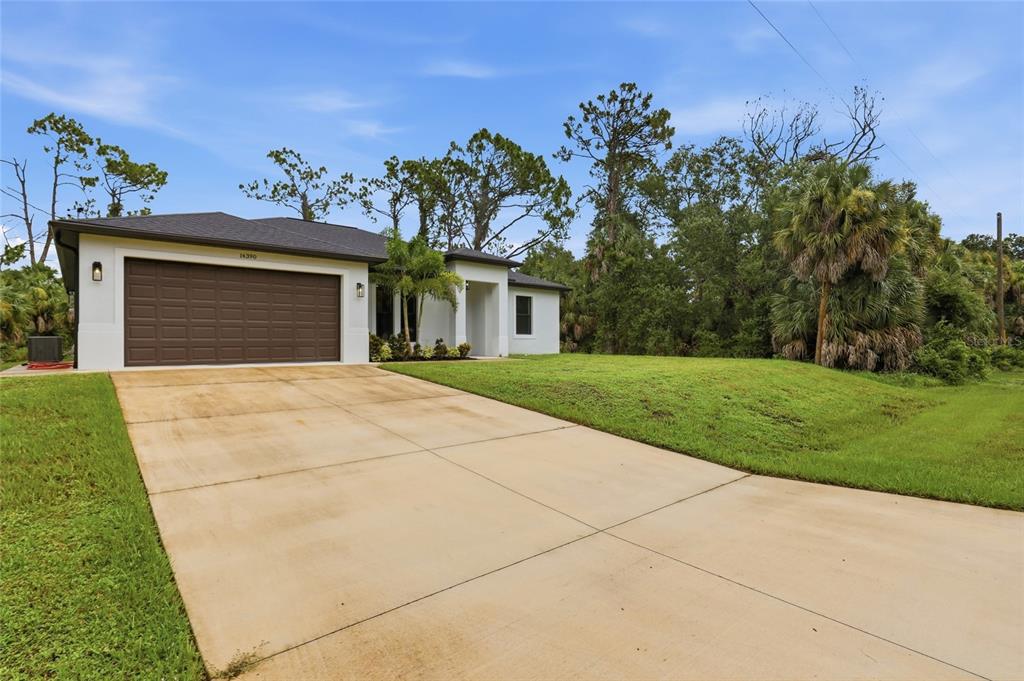 A single-story house with a brown garage door and a concrete driveway under a blue sky — 14390 MADDOCK AVENUE, PORT CHARLOTTE, FL