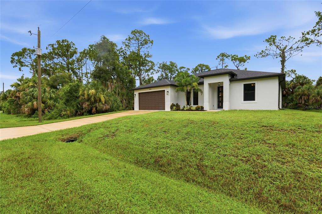 A single-story white house with a brown garage door sits on a grassy lot — 14390 MADDOCK AVENUE, PORT CHARLOTTE, FL