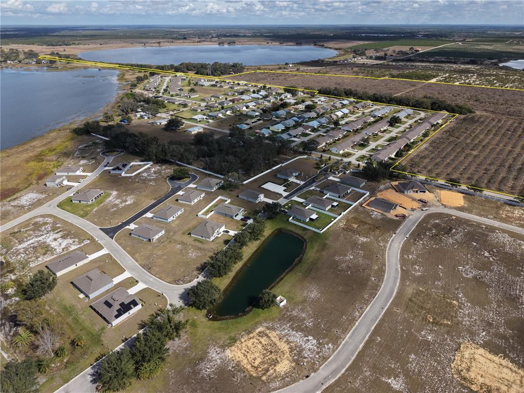 An aerial view shows a residential neighborhood with a lake, a pond, and undeveloped land — 214 E SHOCKLEY ROAD, AVON PARK, FL