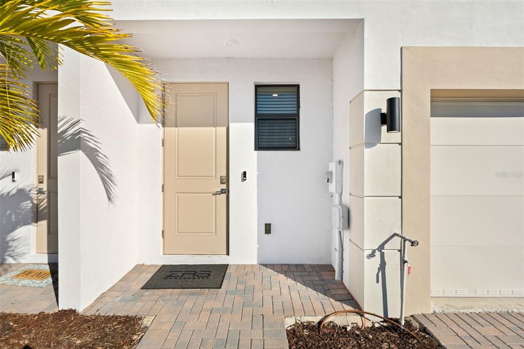 A tan front door with a black doormat sits beside a white wall and garage — 14527 STELLAR PLACE, LAKEWOOD RANCH, FL
