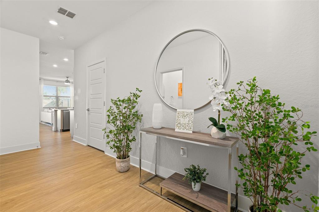 A hallway features light wood-look flooring, a console table with a mirror, and two potted plants — 14527 STELLAR PLACE, LAKEWOOD RANCH, FL