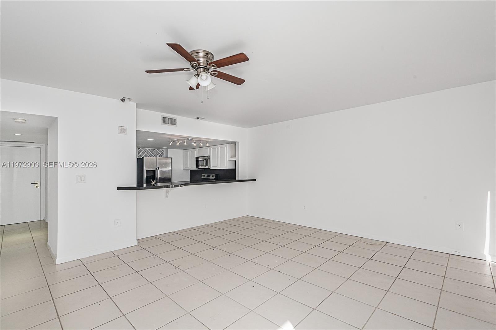 An empty living room with white walls, tile flooring, and a kitchen pass-through window — 555 NE 15th St # 603, Miami FL 33132, MIAMI, FL