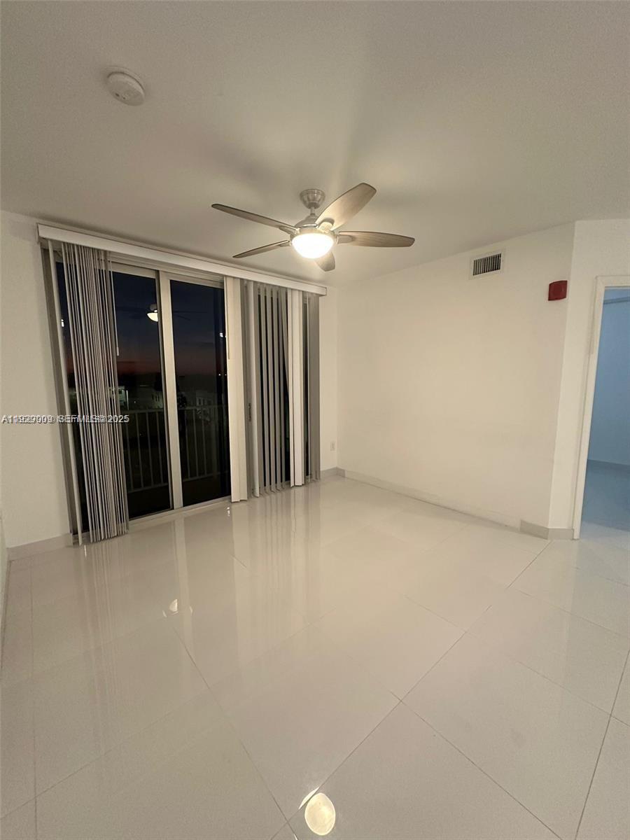 A bright, empty room features white tile floors, a ceiling fan, and sliding glass doors — 2651 NE 212th Ter # 400, Miami FL 33180, MIAMI, FL