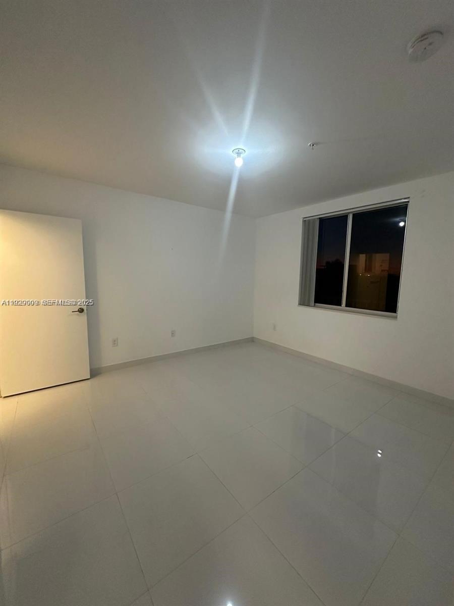 An empty room features white walls, a single ceiling light, and light-colored tile flooring — 2651 NE 212th Ter # 400, Miami FL 33180, MIAMI, FL