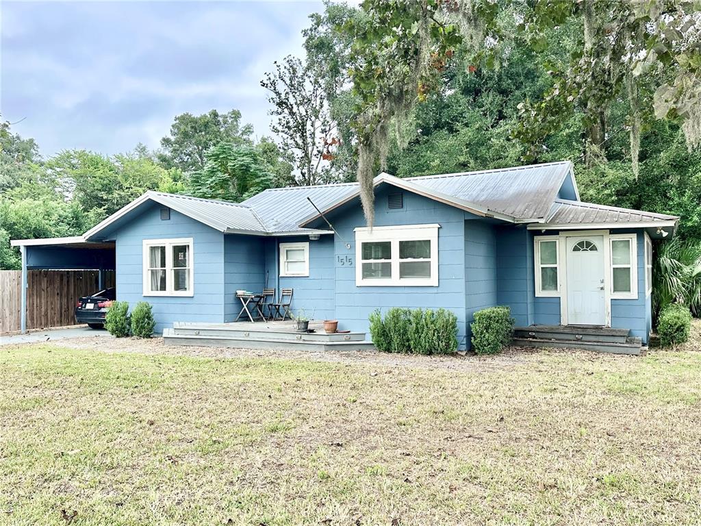 A blue, single-story house with a metal roof and a carport sits on a lawn — 1515 NE 55TH STREET, OCALA, FL