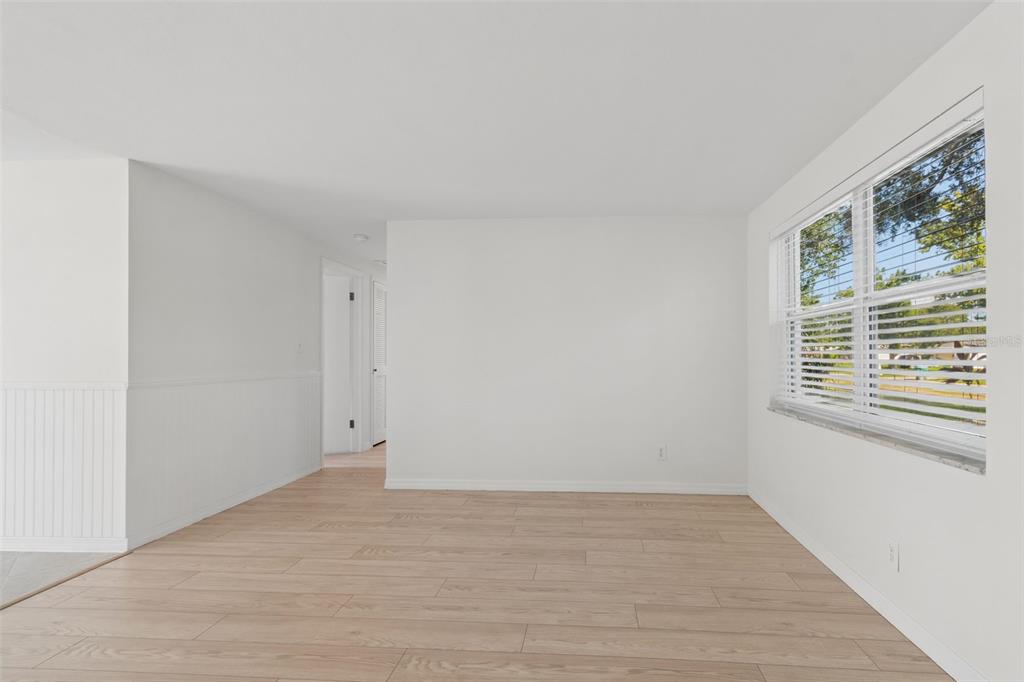 An empty room with light wood-look flooring, white walls, wainscoting, and a large window — 8672 78TH PLACE, SEMINOLE, FL