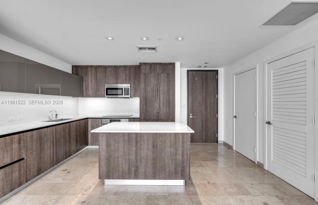 A modern kitchen features wood-grain cabinetry, a white island, and light-colored tile flooring — 88 SW 7TH ST # 2005, Miami FL 33130, MIAMI, FL