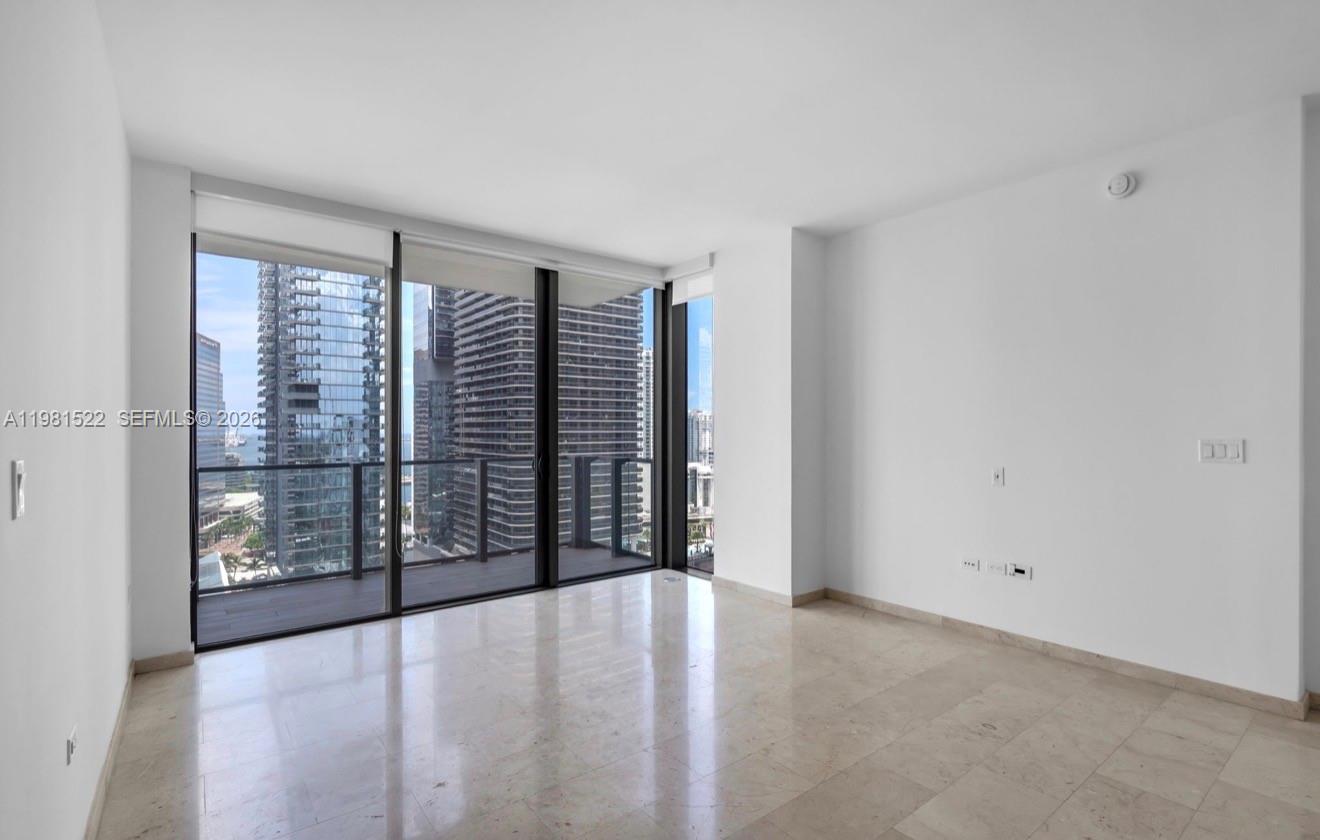 An empty living room features marble floors, white walls, and floor-to-ceiling windows with balcony access — 88 SW 7TH ST # 2005, Miami FL 33130, MIAMI, FL