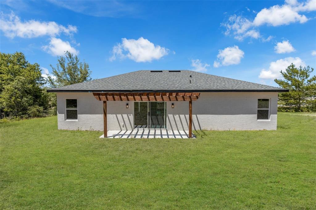 The exterior of a single-story house features a wooden pergola over a concrete patio — 1767 SW 166TH STREET, OCALA, FL