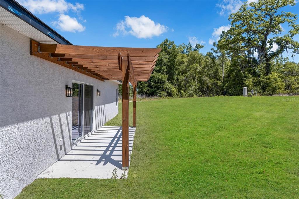 A wooden pergola extends from the side of a white house over a concrete patio — 1767 SW 166TH STREET, OCALA, FL