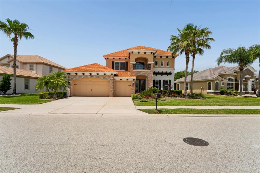 A two-story stucco house with a tile roof, three-car garage, and palm trees in front — 8719 CREEDMOOR LANE, NEW PORT RICHEY, FL