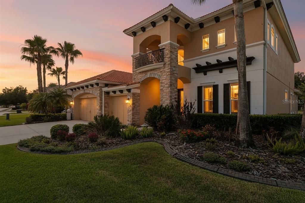 A two-story Mediterranean-style house with a stone facade, tile roof, and attached garage at sunset — 8719 CREEDMOOR LANE, NEW PORT RICHEY, FL