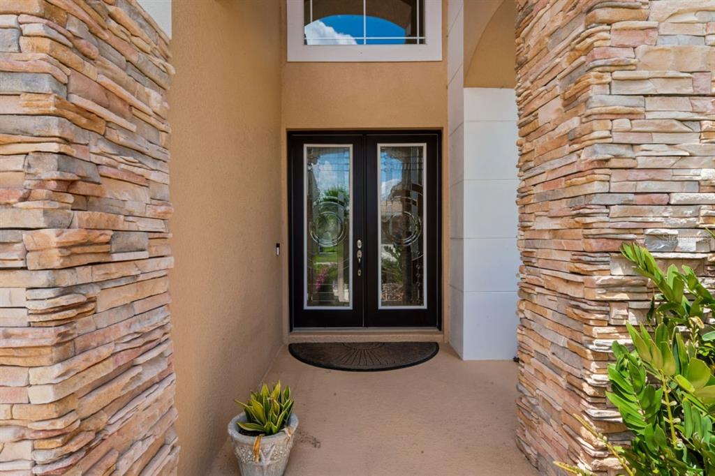 A front entryway features double glass doors flanked by stacked stone columns and a plant — 8719 CREEDMOOR LANE, NEW PORT RICHEY, FL