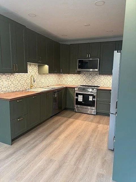 A kitchen features dark green cabinets, wood countertops, a patterned backsplash, and stainless steel appliances — 3053 SW 21st St, Miami FL 33145, MIAMI, FL