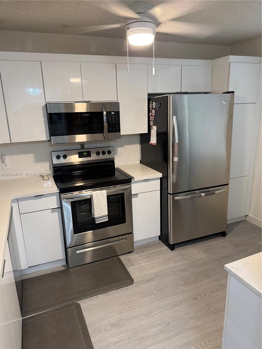 A kitchen features white cabinets, stainless steel appliances, and light wood-look flooring — 10312 NW 24th Pl # 106, Sunrise FL 33322, SUNRISE, FL