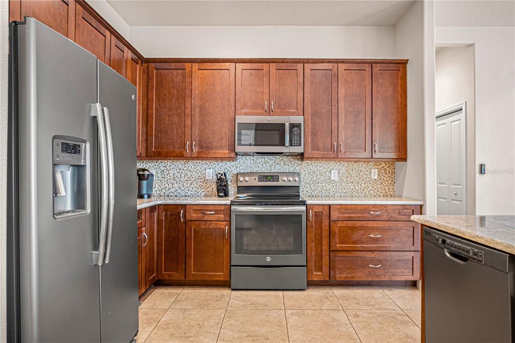 A kitchen features wood cabinets, stainless steel appliances, a tiled backsplash, and granite countertops — 2938 SERENO POINTE DRIVE, TITUSVILLE, FL