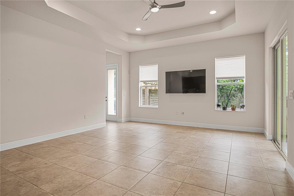 A living room with tile floors, a tray ceiling, a wall-mounted television, and sliding doors — 2938 SERENO POINTE DRIVE, TITUSVILLE, FL